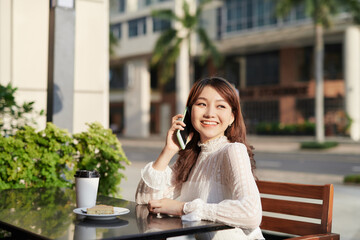 Young and beautiful Asian freelance business woman using a smart phone at the restaurant terrace in the urban city