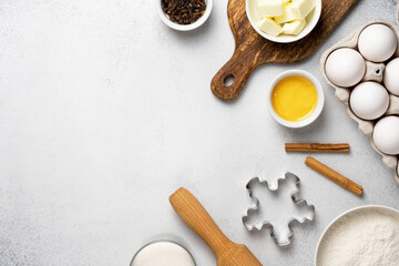 Top view of wheat flour, sugar, rolling pin, cloves, butter, honey, cinnamon sticks, cookie cutter and white eggs on grey background. Flat lay with baking ingredients for gingerbread cookies. 