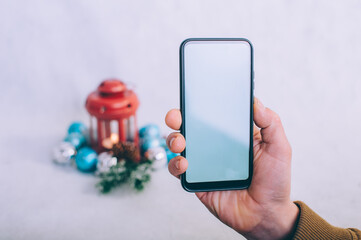 The guy holds a smartphone with a white screen in his hands on the background of a Christmas composition.