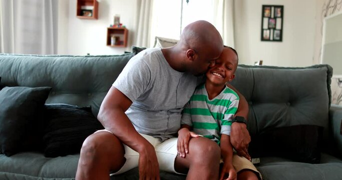 Mixed race father kissing son boy in the cheek at home sofa