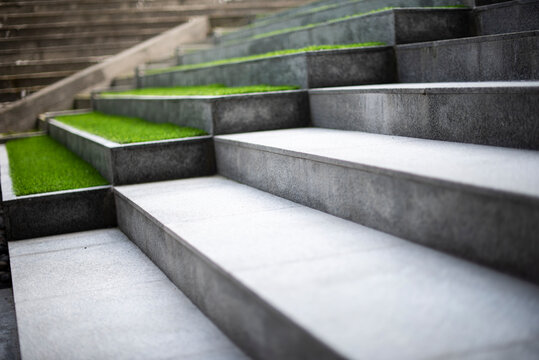 Neat and tidy grey stair steps made of stone and granite tiles with a curb, side by side with green steps in a modern hotel leading to a lobby area, close up.