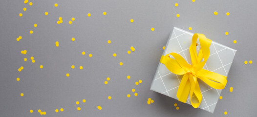 Gift box with yellow ribbon and confetti on ultimate gray paper background. Colors of the 2021...
