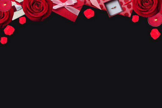 Valentines background with red rose, valentine envelope and petals on the black, flat lay with copy space, top border