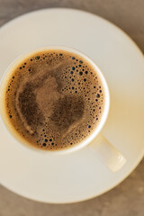 White cup of coffee on saucer on dark stone background. Top view.