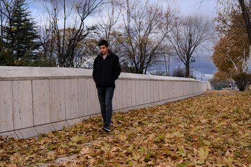 a man walking on fallen leaves in autumn. sycamore leaves are laid on the ground. pensive facial expression.