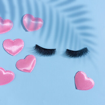 Creative concept beauty fashion photo of lashes extensions with valentine hearts on blue background.