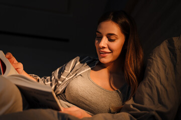 Charming happy woman smiling and reading book while lying in bed