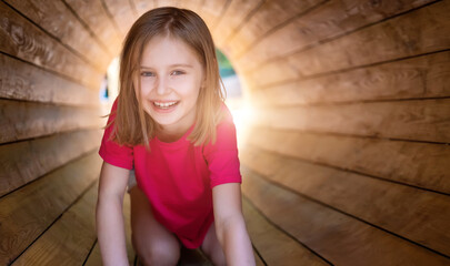 Smiling little girl sitting in wooden pipe in park