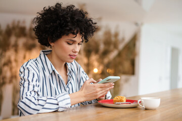 Beautiful woman using mobile phone while drinking coffee with cake