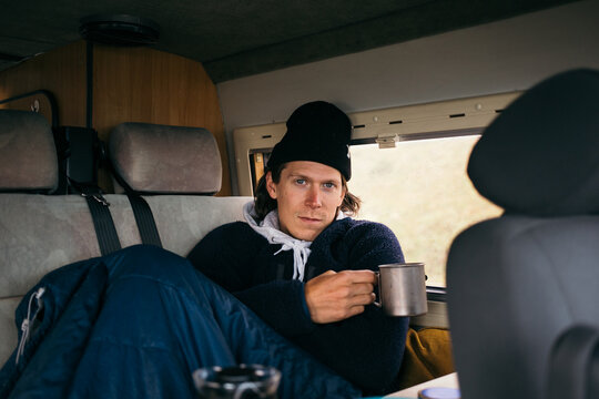 Handsome young man, traveller on road trip, sit inside camping van on rainy day. Cosy comfortable setup in custom camper trailer or van. Millennial travel trend, adventure on the road. Cosy camping
