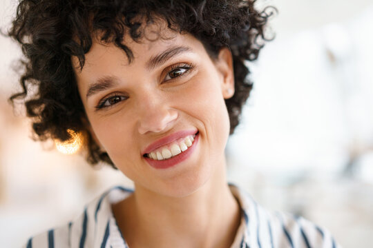Beautiful curly happy woman smiling and looking at camera indoors