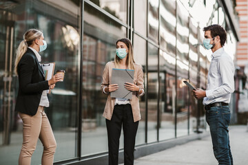 Three employers standing in social distance wearing face mask looking at each other and talking
