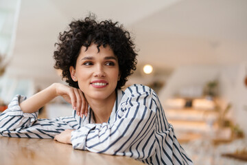 Beautiful happy curly woman smiling on camera while sitting in cafe