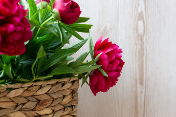 flowers of pink red peonies in wicker basket on wooden table against wooden background