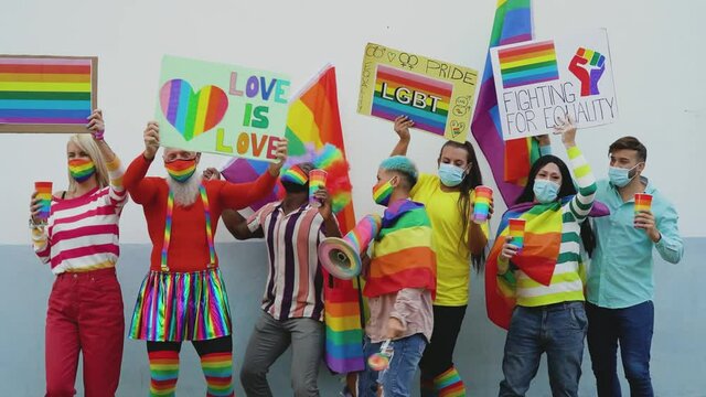 Happy Multiracial people wearing face mask celebrating at gay pride festival during corona virus - Group of friends with different age and race dancing together and fighting for gender equality