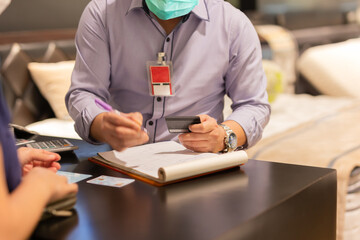 Seller in protective mask hand holding credit card and writing card detail.
