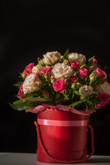 Cute bouquet of pink and beige roses in a red box on a black background. Selective soft focus.