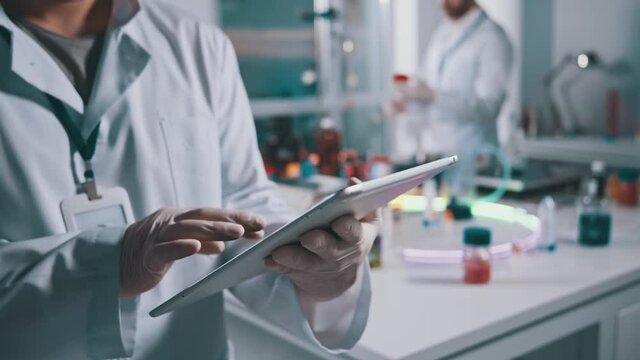 Close-up of lab worker using digital tablet at workspace. Male scientist expert browsing technology device collaborating in medical research laboratory.