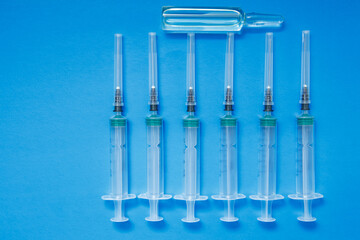An ampoule with a vaccine and syringes on a blue background. The concept of vaccination against coronavirus.