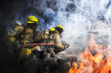 Firemen wearing yellow clothes extinguish fires that are extremely hot. There are both flames and smoke.