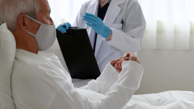 ベッドに横になり医師の診察を受けるマスクをつけた日本人シニア男性
