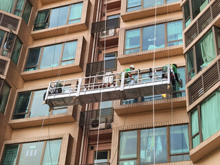 Two Professional workers use a suspended cradle or steeplejack to access and clean windows of...