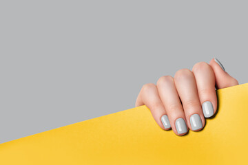 Female hand holds a sheet of paper and demonstrates a gray manicure. Gray, yellow background with place for text.