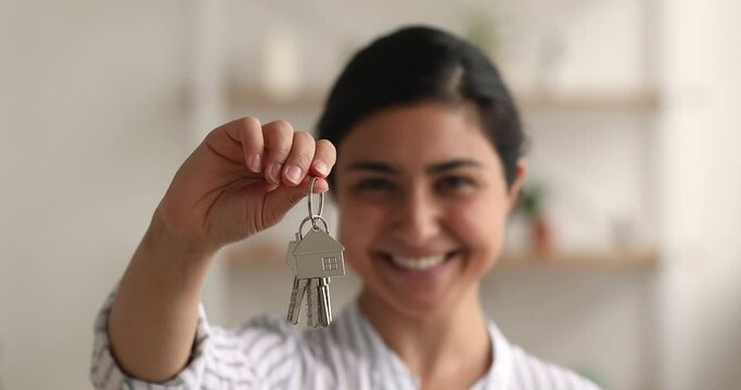 Close up view female hand holding keys from new house. Happy young Indian woman glad for first new home purchase. Satisfied smiling client buying modern flat, real estate agent sell apartment concept