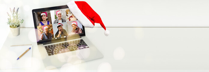 Computer in cozy room with hanging red hat and with Santa Claus on screen wishing Merry Christmas and Happy New Year online