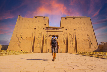 A young tourist entering the Temple of Edfu in the city of Edfu at sunset, Egypt. On the banks of the River Nile, geco-Roman construction, temple dedicated to Huros - obrazy, fototapety, plakaty