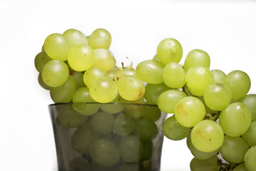 On a white background in a black transparent bowl is a bunch of green grapes. Isolated.