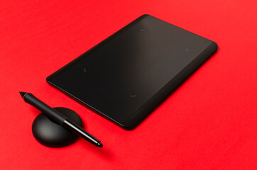 Black graphics tablet, stylus on the red background