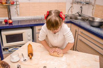 Cute funny girl learns to prepare Christmas gingerbread cookies in bright cozy kitchen, kneads...