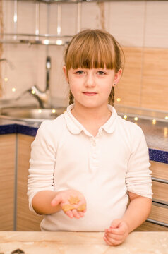 Cute happy girl learns how to cook Christmas gingerbread cookies in bright kitchen, kneads dough, shows future cookies