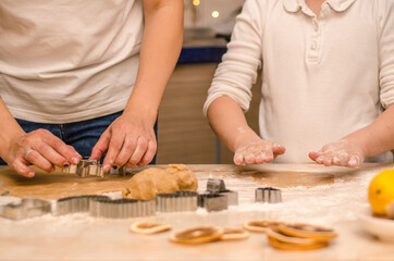 Hands of mother and daughter prepare gingerbread cookies for christmas, they roll out dough and cut cookies