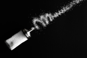 White sugar pours out of sugar bowl on dark black background