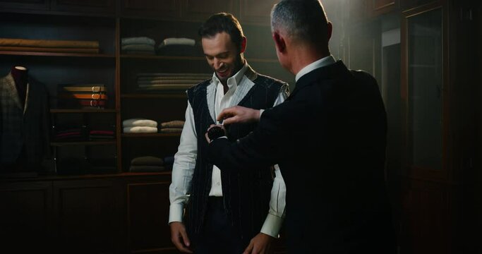 Cinematic shot of professional tailor taking measurements of client for creation custom tailored suit in a luxury tailoring atelier. Concept of fashion, handmade, hand craft, couturier and business