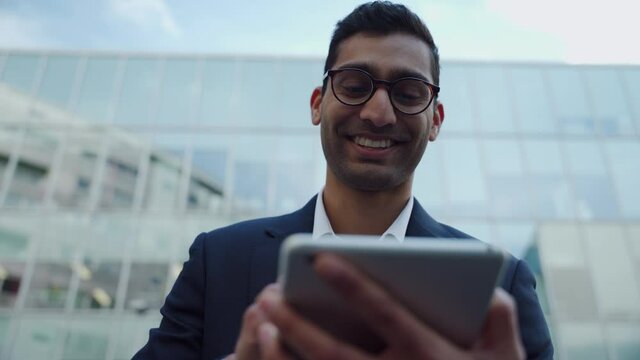 Mixed race business man typing on digital tablet smiling standing outside work office