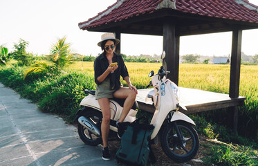 Fototapeta na wymiar Millennial female user checking location information during online GPS tracking via modern cellphone gadget, travel girl resting on rent moped connecting to roaming internet for browsing website