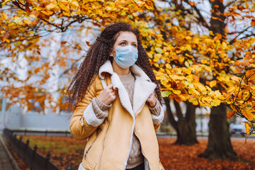 Beautiful afro haired woman wearing protective medical face mask stand on the street of city....