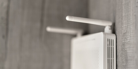 white colored wifi router with long antenna tendrils hangs on wooden wall of home or office room