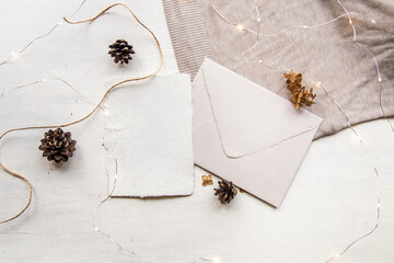 Christmas wish list concept. Blank letter mock up on handcrafted paper. Letter envelope, pine cones, craft thread and candle. Cozy hygge style. Flat lay, top view.