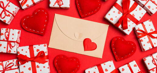 Top view of craft envelope, white gift boxes and red textile hearts on colorful background. Valentine's Day concept