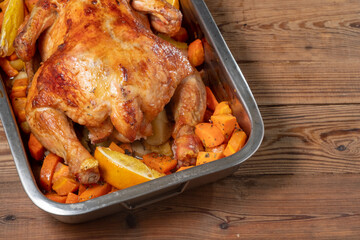 Whole baked chicken with carrots and oranges on a wooden table. Close-up and top view