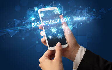 Female hand holding smartphone with BIOTECHNOLOGY inscription, modern technology concept