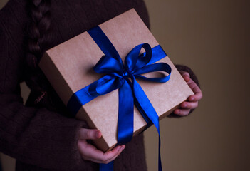 young girl in warm cashmere sweater is holding a gift box with blue ribbon bow - close up, winter holidays and family warm time together
