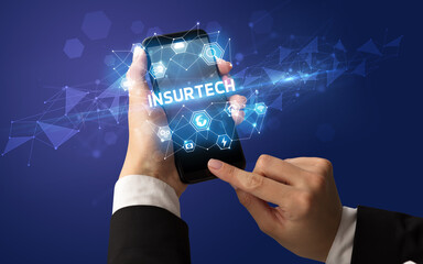 Female hand holding smartphone with INSURTECH inscription, modern technology concept