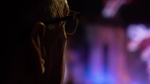 film grain. senior with glasses at home watching tv news. back view. concept people watch news on tv every day