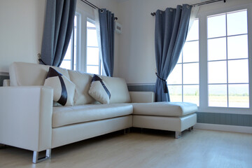 Living room inside the house with white leather sofa in the middle of a large window. And has a light gray curtain