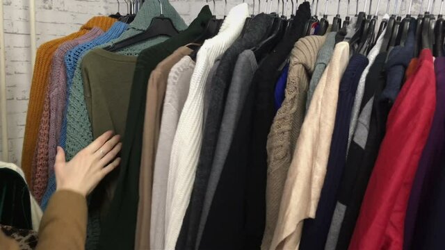 A young woman rummages through a rack of secondhand sweaters, thrift shop, 4k footage